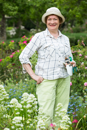 smiling senior woman gardener holding horticultural tools in garden on sunny dayの写真素材