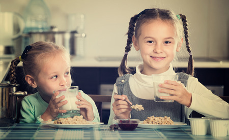 Portrait of happy smiling cute little sisters eating porridge in kitchenの写真素材
