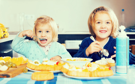 Happy smiling cute little girls with cream desserts at home kitchenの写真素材