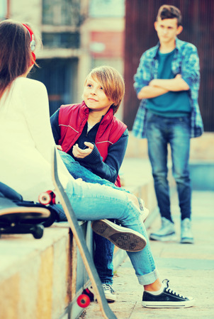 Upset boy and happy couple of teens apart on the streetの写真素材