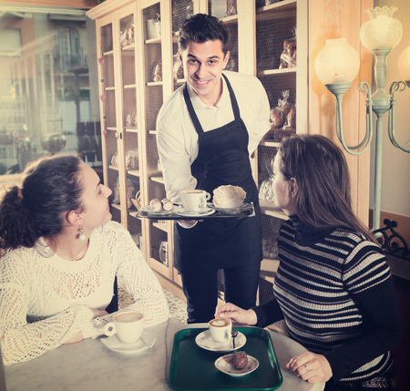 Portrait of smiling girls chatting in coffee-house and cheerful waiterの写真素材