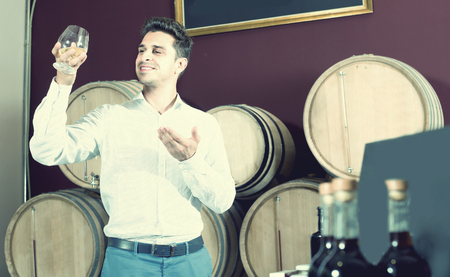 cheerful smiling adult man having glass with brandy in winery storeの写真素材