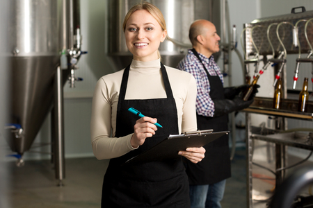 Pretty woman wearing uniform standing among brewery stainless equipmentの写真素材