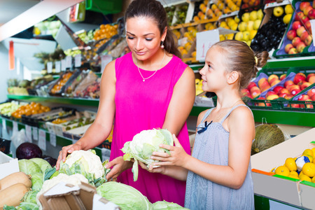 positive young woman with girl buying cabbage on marketplaceの写真素材