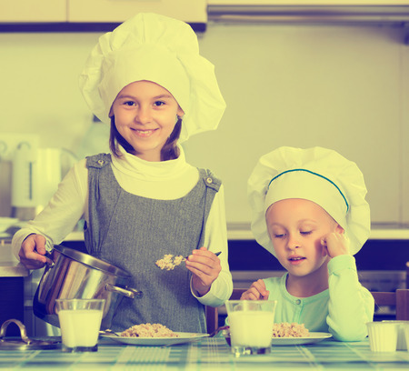 Two happy small girls eating healthy oatmeal in domestic kitchenの写真素材