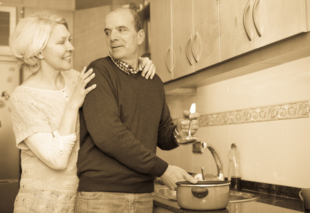 Senior husband helping smiling wife to cook indoorsの写真素材
