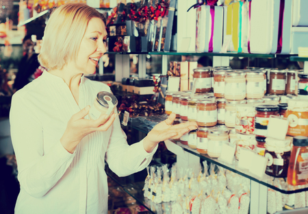 Smiling mature blonde consumer buying jar with white honey in cafeの写真素材