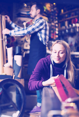 Young smiling female customer examining belts in leather workshopの写真素材