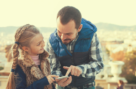 Young father and girl looking at guide in phone during sightseeing tourの写真素材