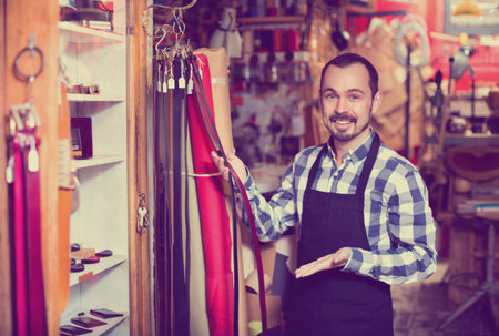 Smiling cheerful male worker showing new belts in leather workshop
