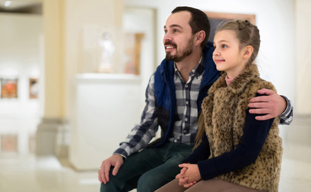 happy russian father and daughter looking at paintings in halls of museumの写真素材