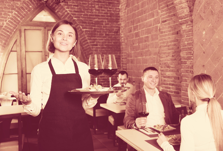 positive woman waiter demonstrating country restaurant to visitorsの写真素材