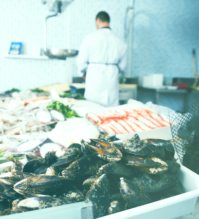 attentive seller standing with his back to counter and cuts fish in the shopの写真素材