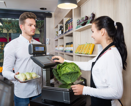 Smiling female seller assisting customer to weigh cabbage at a grocery shop. Focus on man