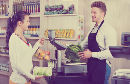 Male shopping assistant helping customer to weigh purchases in the grocery shop. Focus on manの写真素材