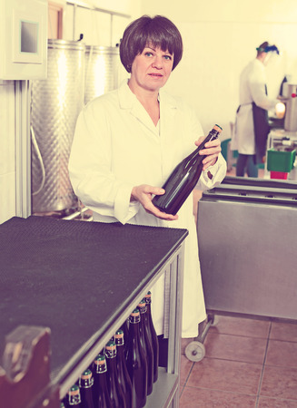 Positive female employee with wine bottles at sparkling wine factoryの写真素材