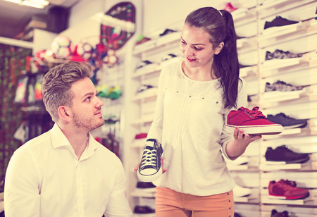 Happy woman seller assisting man in choosing sneakers in sports storeの写真素材