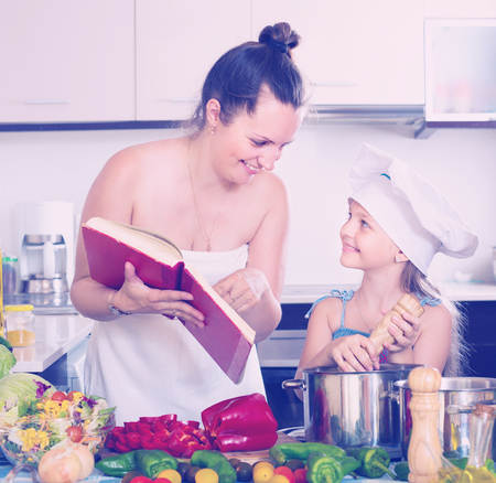 Little girl with mom learning new recipe from cookery bookの写真素材