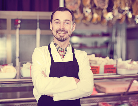 Young male seller offering displayed sorts of meat in butchers shopの写真素材