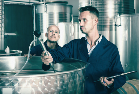 Portrait of young man expert wearing coat standing and taking off data from equipment in wineryの写真素材