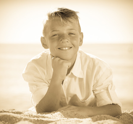 Portrait of smiling boy in elementary school age lying on beach on sunny weatherの写真素材