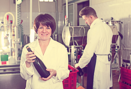 Smiling woman worker displaying wine bottle at sparkling wine factoryの写真素材
