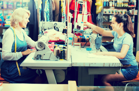 Two smiling women tailors working with sewing machines at studioの写真素材