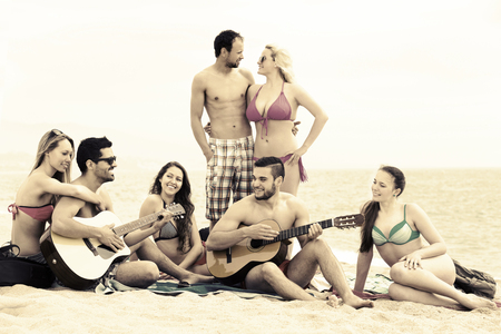Cheerful friends relaxing on sand at beach with guitar and singing. Selective focusの写真素材