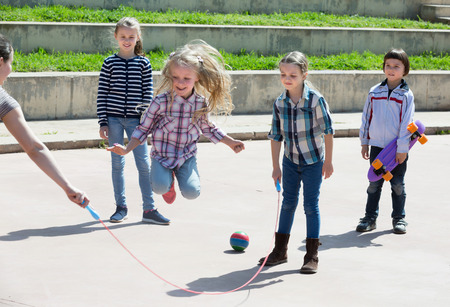 Positive girl jumping while jump rope game with friends outdoorの写真素材