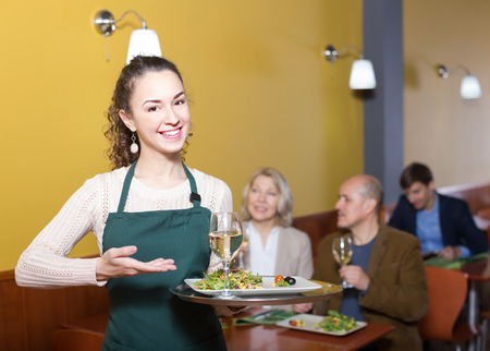 Smiling young waitress greeting customers at table in restaurantの写真素材