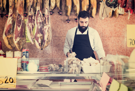 Male shop assistant 25-30 years old carving meat to sell in butchers shopの写真素材