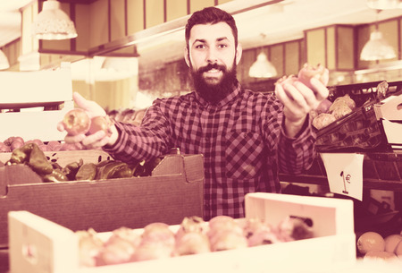 Smiling arab man seller showing persimmons in grocery shopの写真素材
