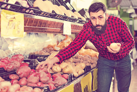 Young  positive male seller offering potatoes in grocery shopの写真素材