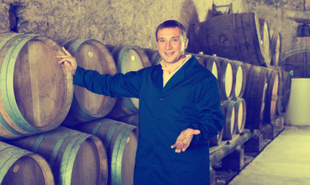 Man wine house technician working in storage with wooden barrels
