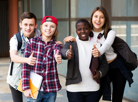 Positive group of teens posing outside school with papers for studyの写真素材