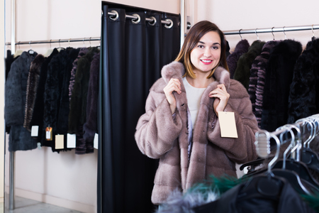 Pretty girl customer trying on new fur coat in womens cloths storeの写真素材