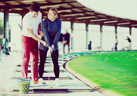 Cheerful man golf trainer showing woman player how to hit ball rightlyの写真素材