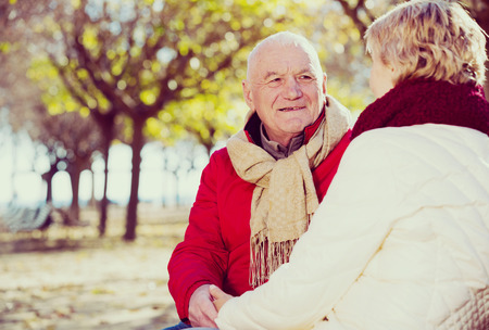 Senior couple sitting on bench and talking in parkの写真素材