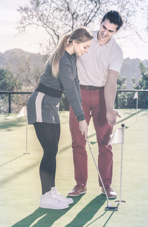 Man 30-35 years old is training woman 25-29 years old to play golf and hit ball correctly.の写真素材