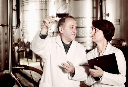 Expert and wine maker  standing and estimate quality of red wine in wineglass