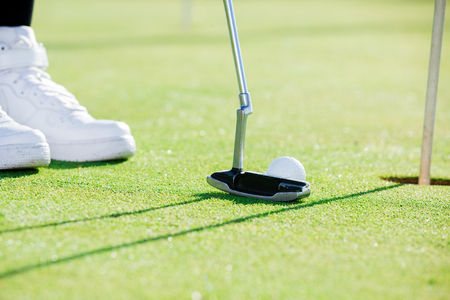 Golf player using golf club to propel ball towards holeの写真素材