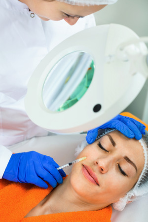 Diligent smiling woman doctor making beauty injection to young female clientの写真素材