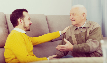 Old father and son are friendly conversation sitting at home on sofaの写真素材