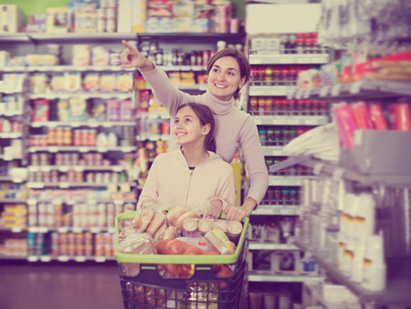 Smiling woman with girl shopping with shopping cart in supermarketの写真素材