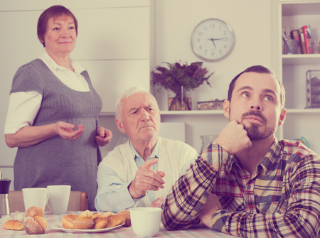 Father and mother having disagreement with adult son at homeの写真素材