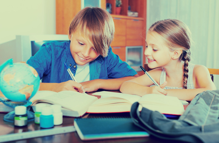 Smiling teenage boy and cute little girl studying with books indoorsの写真素材