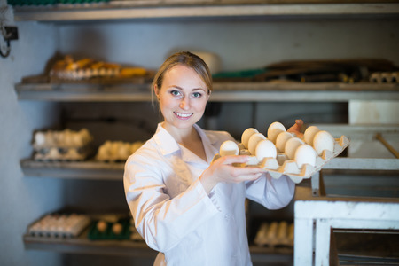 Young woman holding carton tray with fresh eggs on farmの写真素材