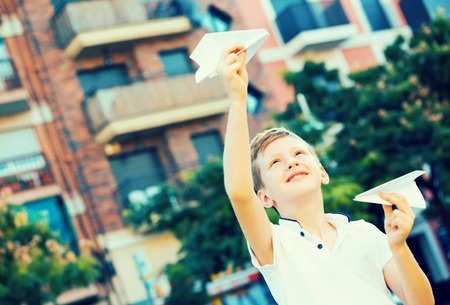 portrait of glad boy throwing  paper airplanes in park on summer dayの写真素材