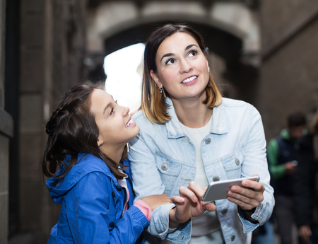 Cheerful mother and daughter reading guide in phone during sightseeing tourの写真素材