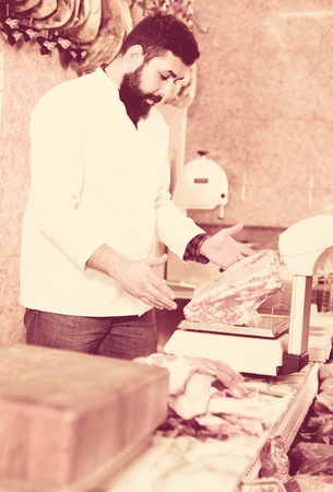 Male shop assistant measuring meat to sell in butchers shopの写真素材